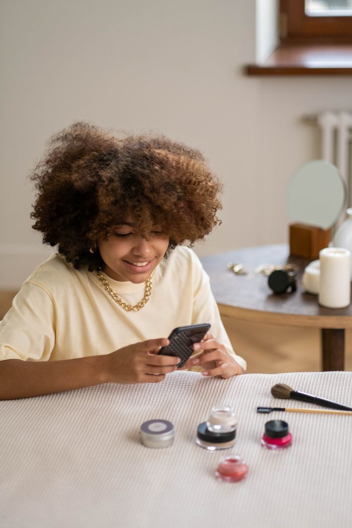 A woman with afro hair reviews beauty products in an indoor setting.