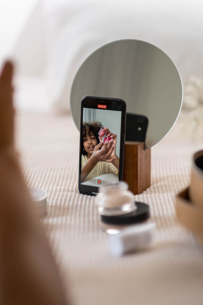 Young woman vlogger reviews beauty products in front of a smartphone, capturing engaging content for her audience.
